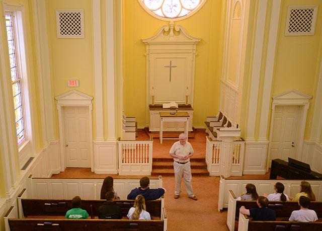 Male professor addresses a small group of students int he college chapel